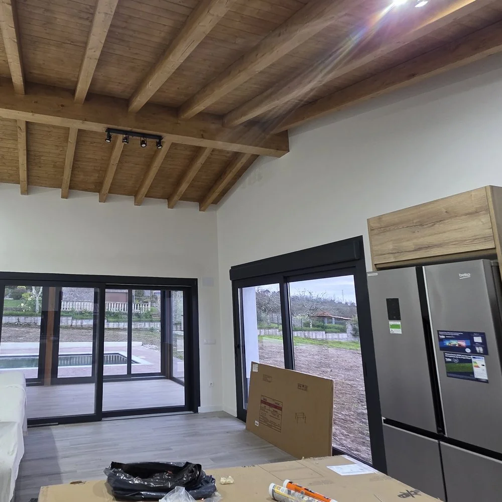 Salón de una vivienda unifamiliar con vigas de madera vistas, paredes blancas y puertas correderas al jardín