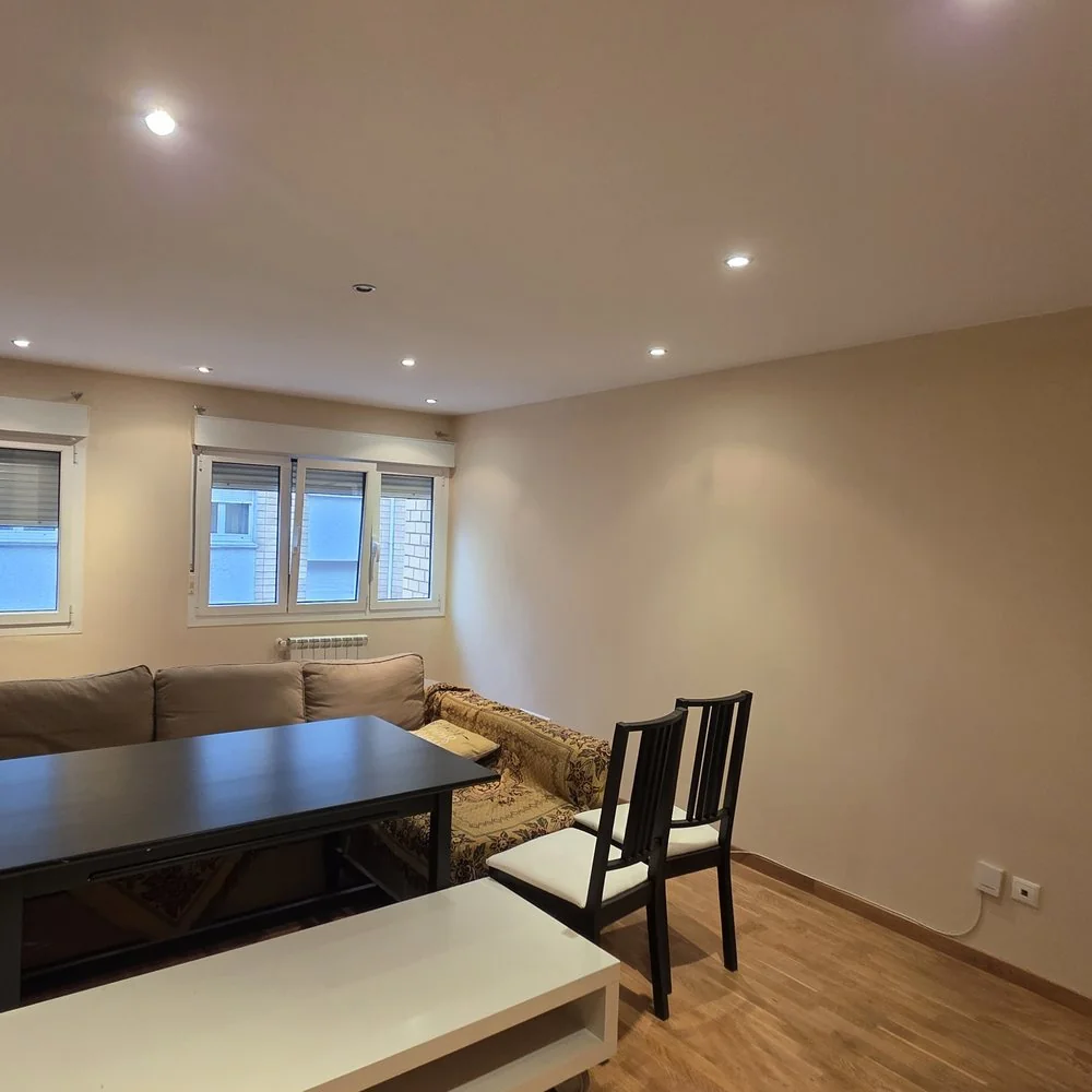 Salón-comedor con las paredes en tono beige, focos empotrados y suelo de madera