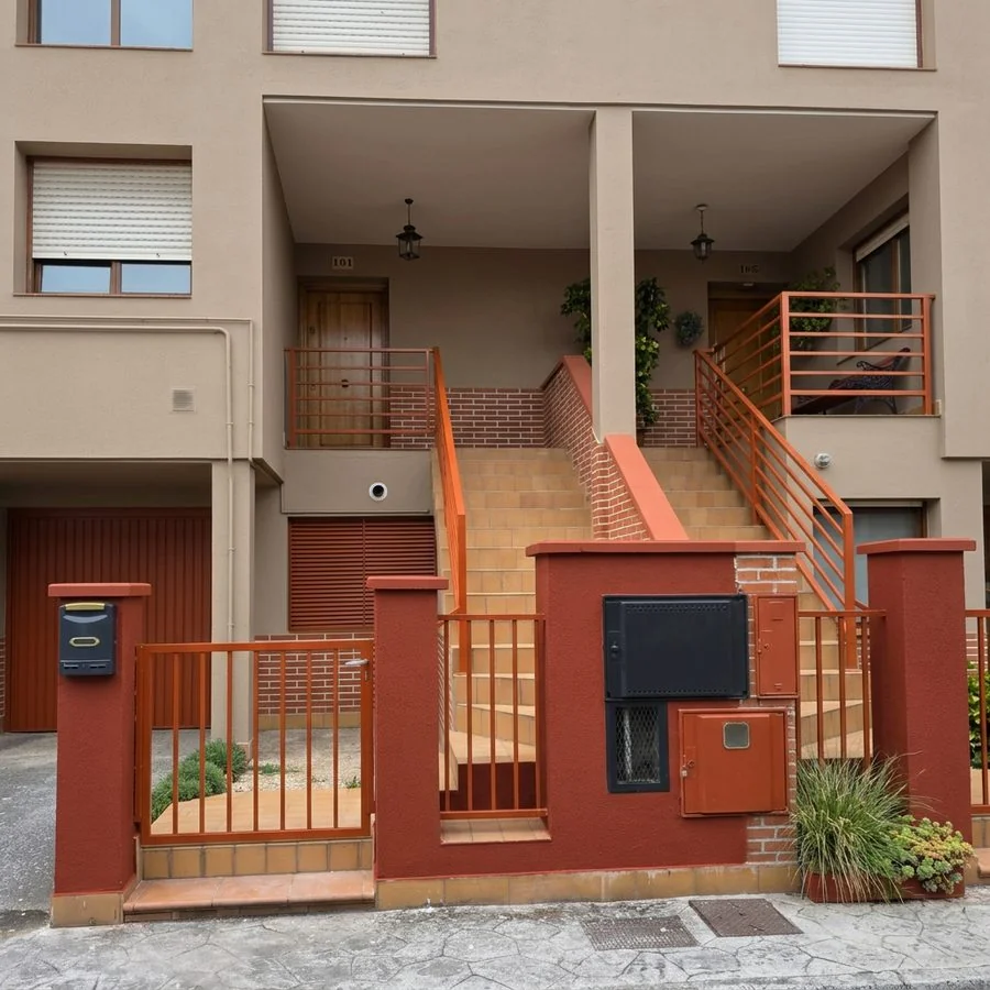 Vivienda adosada en La Fresneda, Siero, con la fachada reparada con mortero y pintada, y barandillas en naranja